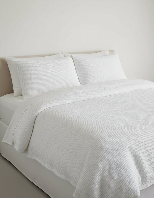 A folded white linen waffle duvet cover set against a neutral background.